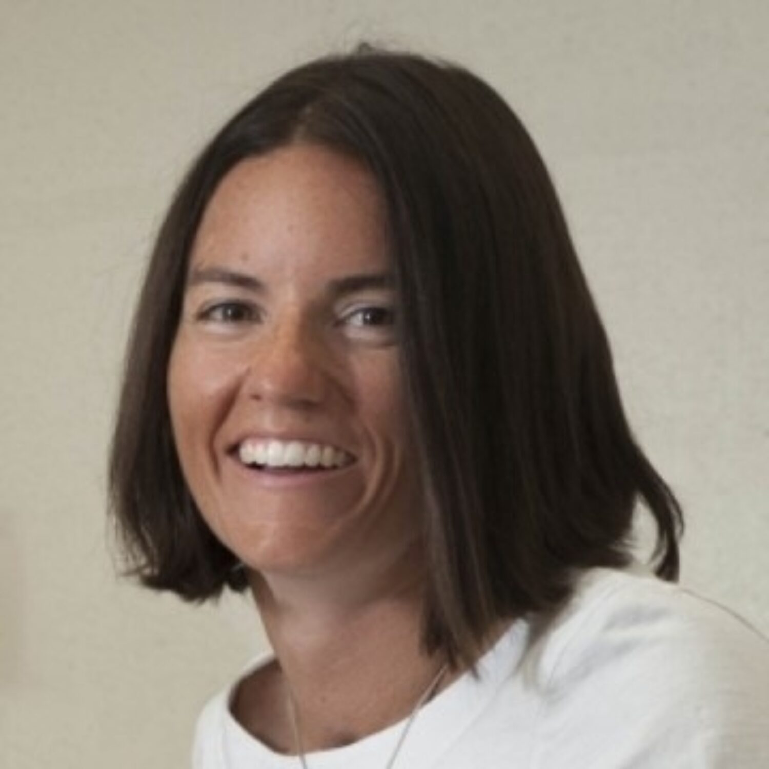 A person with shoulder-length brown hair and a white shirt smiling.