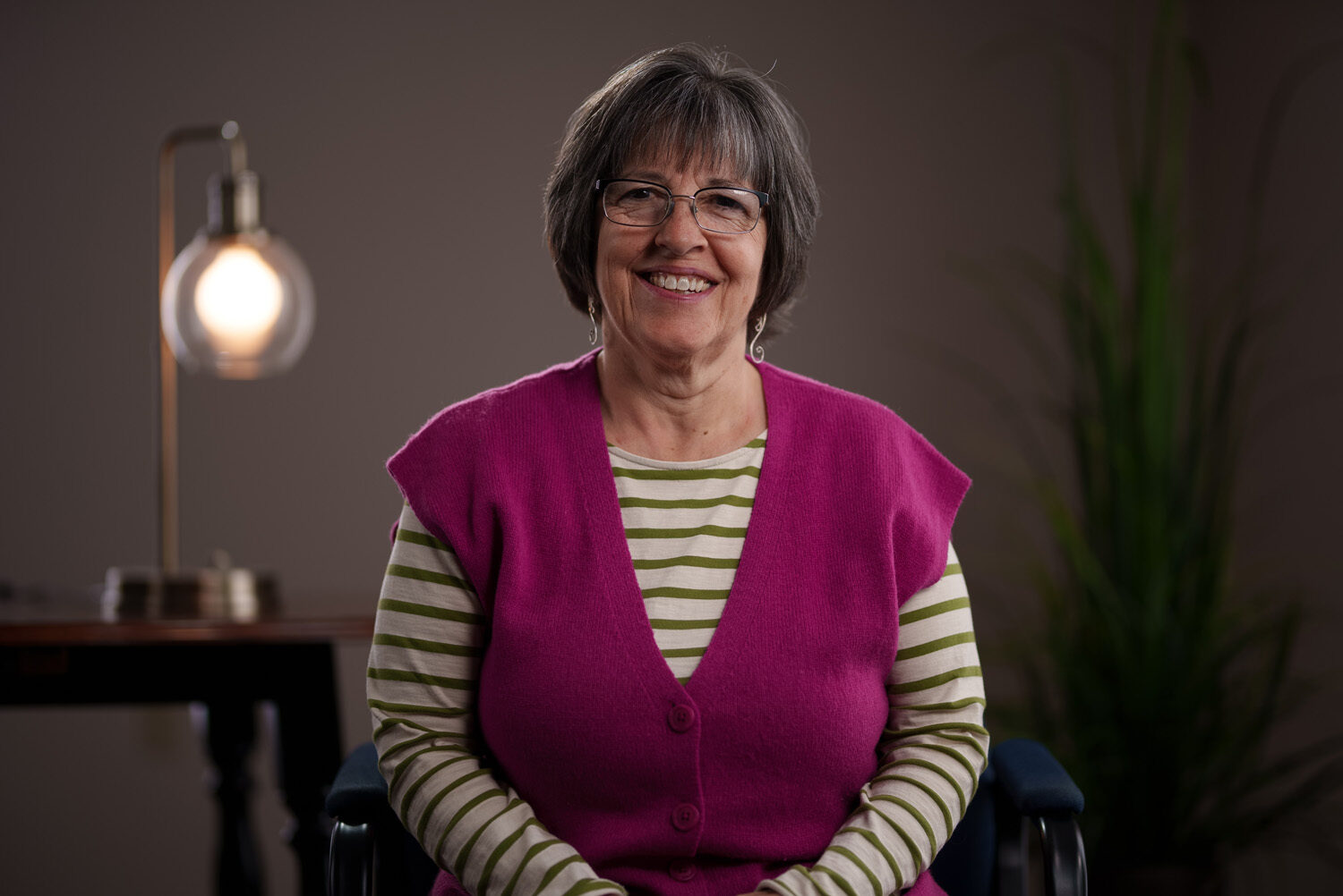 A woman in a wheelchair smiling in front of a lamp.