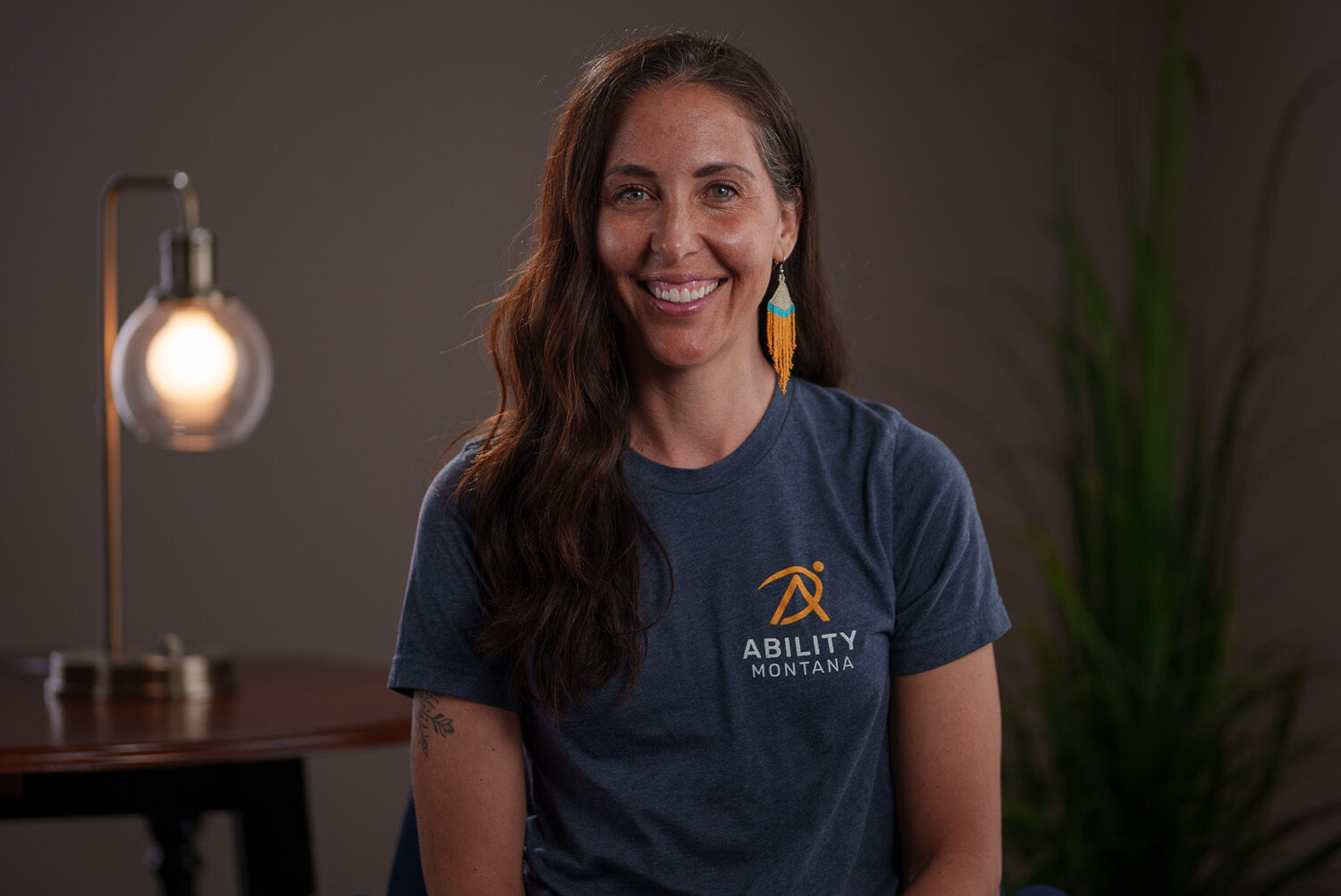 A woman wearing a blue t - shirt smiles in front of a lamp. profile picture