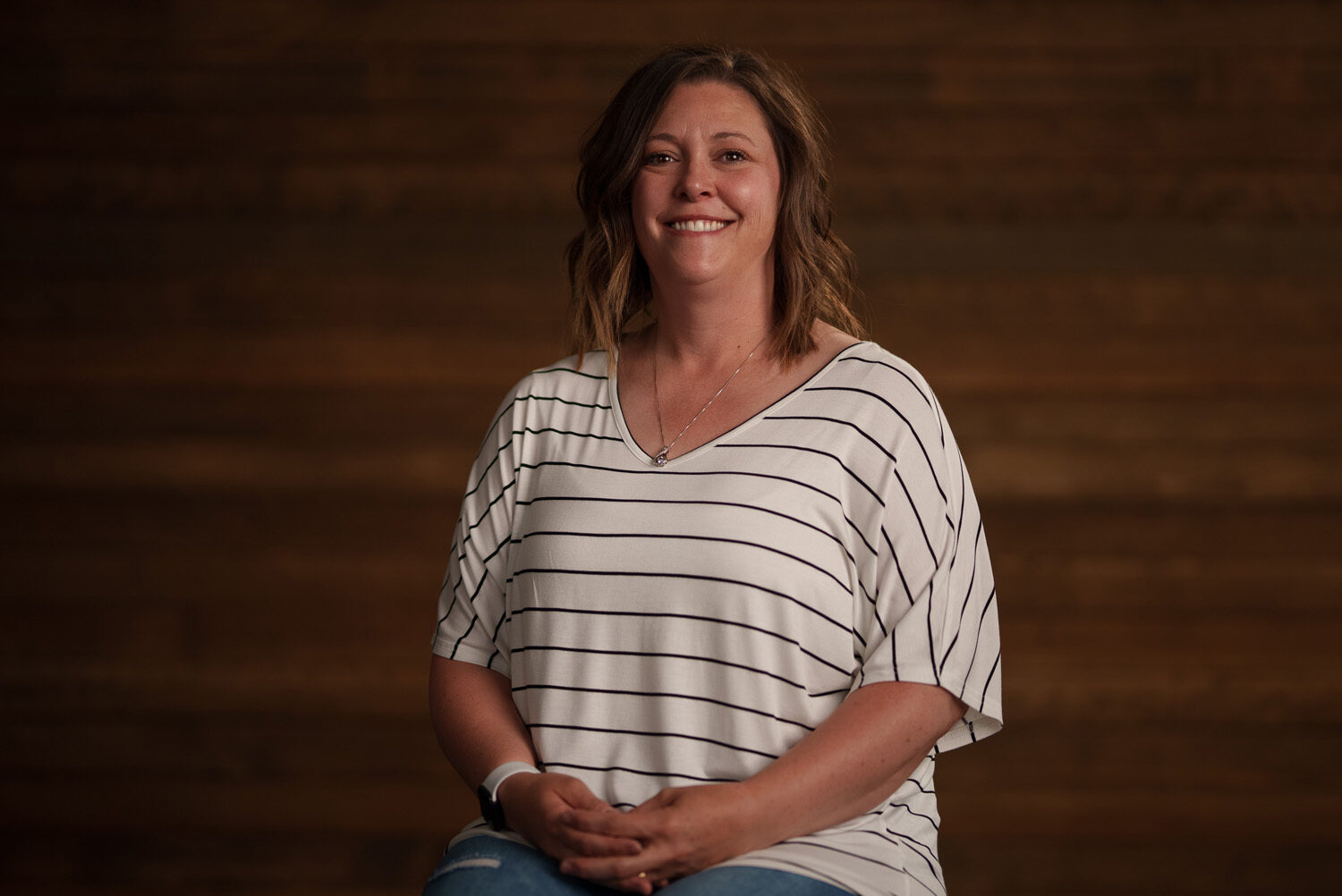 A smiling woman in a striped shirt sitting on a wooden floor. profile picture