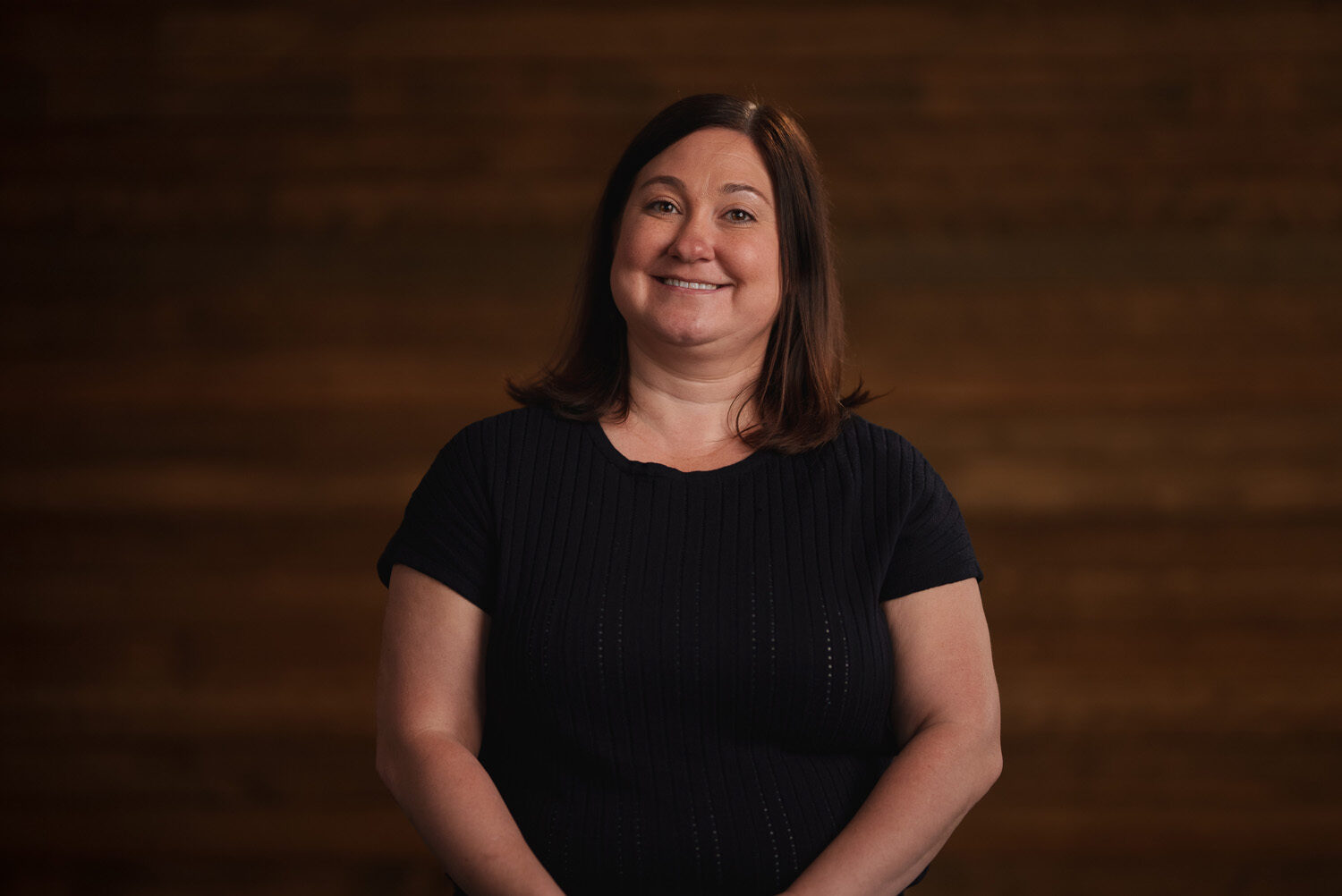 A woman smiling in front of a wooden background. profile picture