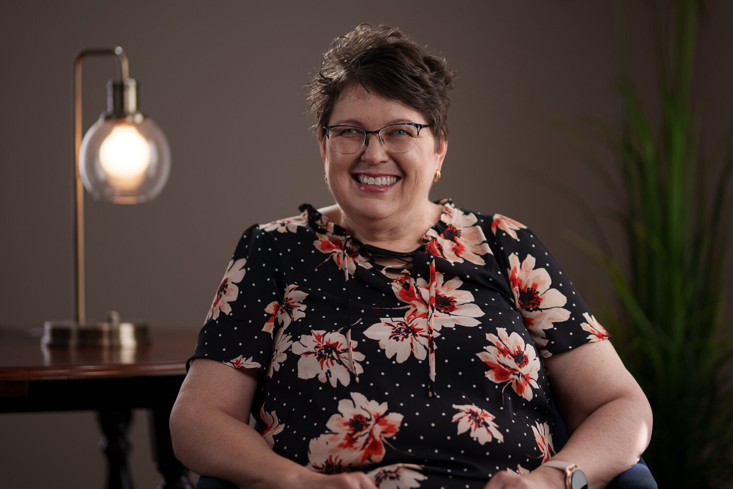 A smiling woman in a floral dress sitting in front of a lamp. profile picture