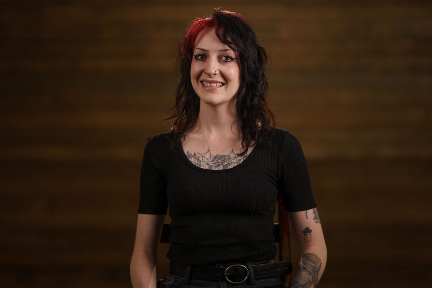 A woman with tattoos standing in front of a wooden background. profile picture