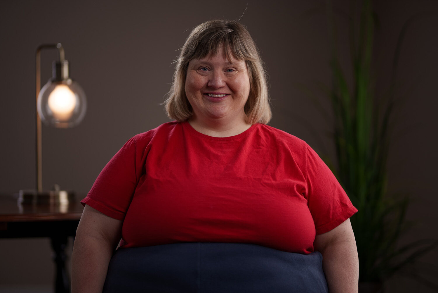 A woman in a red t - shirt standing in front of a lamp. profile picture
